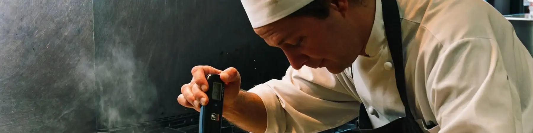 Chef in kitchen whites checking the internal temperature of cooked chicken with a digital probe thermometer in a commercial kitchen